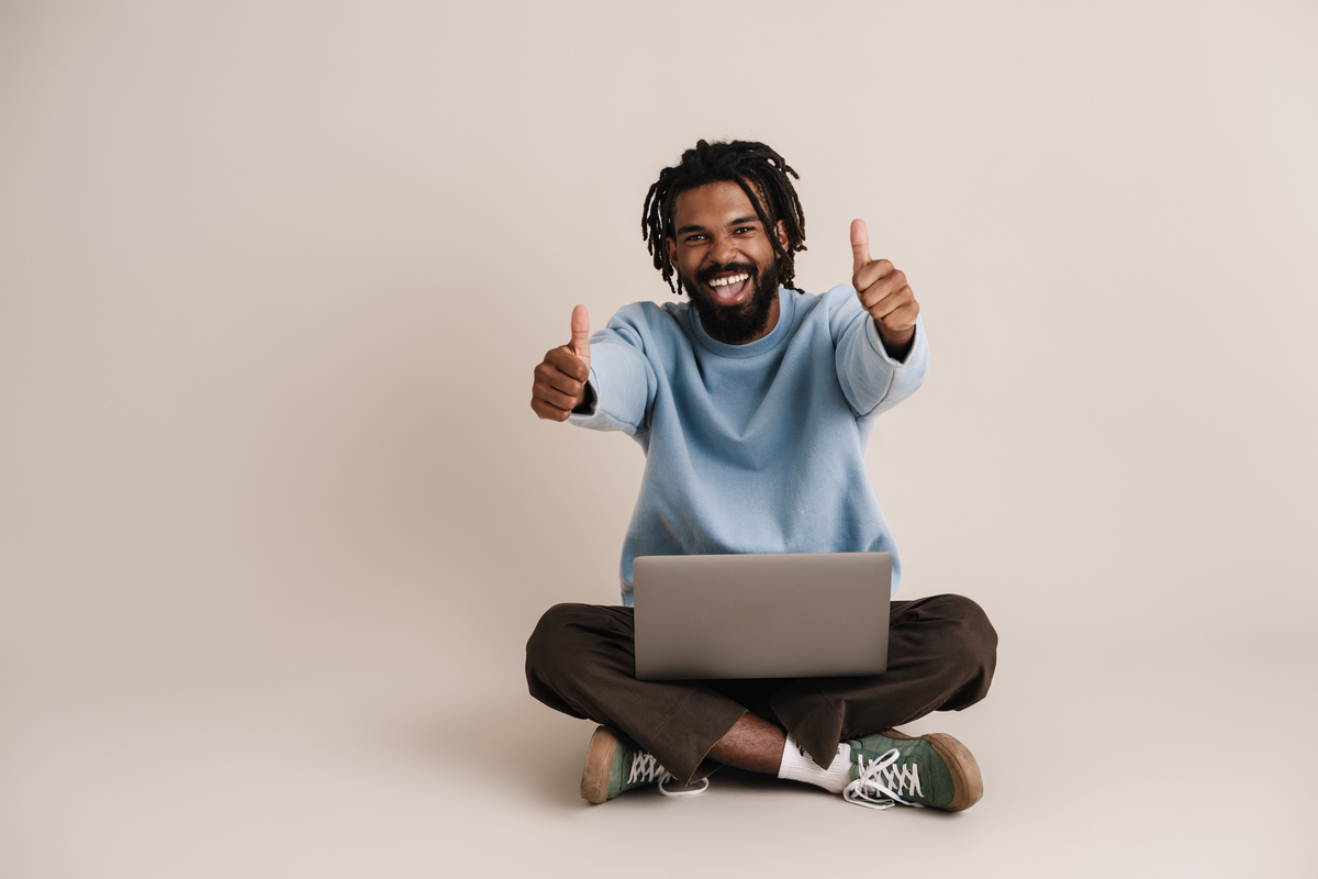 Excited African American Guy Showing Thumbs up While Sitting with Laptop
